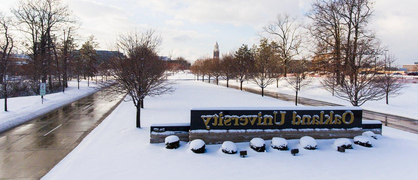 An Oakland University sign at the entrance to campus with snow on the ground.